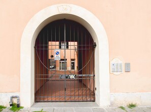 Une entrée fermée par un portail, agrémentée d’un panneau indiquant un numéro, d’un panneau interdisant le stationnement et d’une boîte d’alarme incendie.