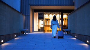 A person walking towards a building entrance with a suitcase, benches, and a well-lit interior visible. - OMO5 Kyoto Sanjo by Hoshino Resorts (Kyoto)