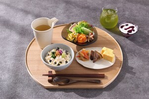 Una bandeja de madera con un tazón de arroz, un plato de verduras y tofu, un vasito de sopa, una taza de té y un vaso de bebida verde.