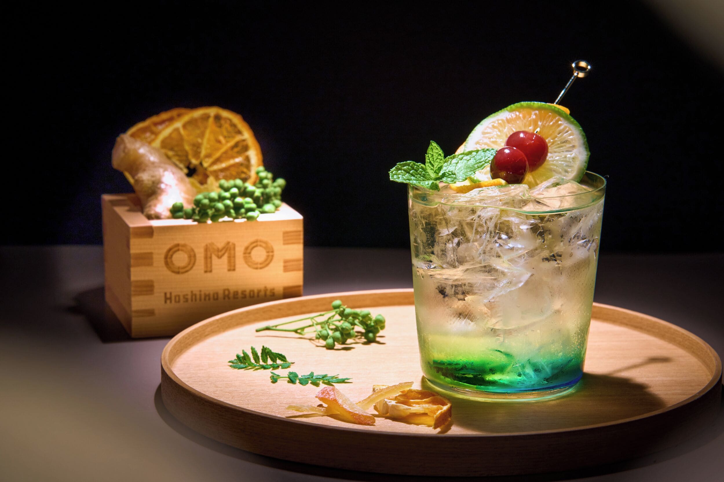 A cocktail glass with a lime slice and mint garnish on a wooden tray.