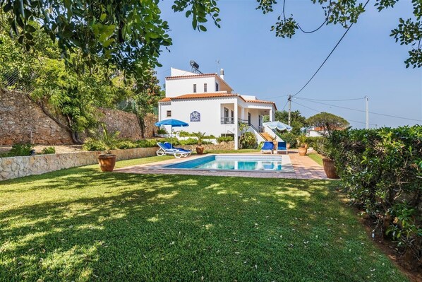 A two-story house with a swimming pool, surrounded by a well-maintained lawn and potted plants.