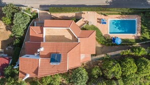 Vista aérea de una casa con piscina, un patio cubierto y un techo de tejas rojas.