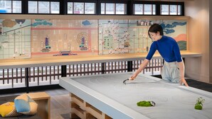 A person interacting with a large interactive map in a room with a view of a cityscape through large windows. - OMO3 Kyoto Toji by Hoshino Resorts (Kyoto)