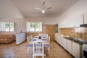 A dining area with a table set for four, a ceiling fan, and a kitchen with patterned tiles and cabinets.