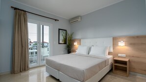 A modern bedroom with a large bed, sliding glass doors to a balcony, a small bedside table, and a wall-mounted air conditioner.