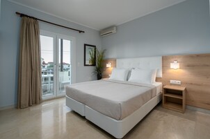 Un dormitorio moderno con una cama grande, puertas de vidrio correderas a un balcón, una mesita de noche pequeña y un aire acondicionado instalado en la pared.