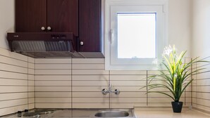 A compact kitchen with dark wooden cabinets, a white refrigerator, a built-in stove, a window, and a potted plant.
