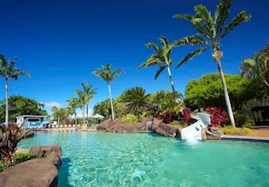 A clear pool surrounded by palm trees and rocks, with a lounge area in the background. - KP169 Ground FL Beachside | Pool•AC•Ocean (Koloa)