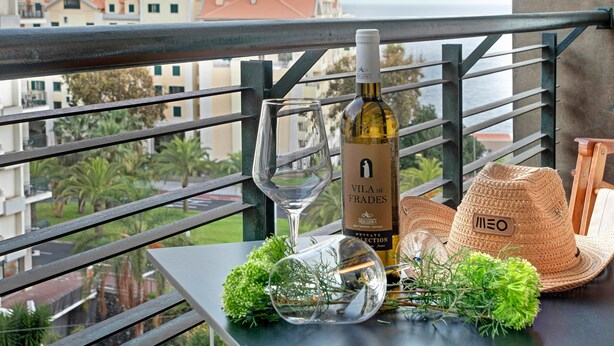 Un balcon avec une table, une bouteille de vin, un verre et un chapeau de paille.