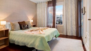 Une chambre d’hôtel avec un lit, deux lampes de chevet, une fenêtre avec des rideaux et une vue sur les bâtiments environnants.