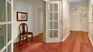 Un couloir intérieur avec un plancher en bois, une porte blanche dotée de panneaux de verre et un tableau encadré accroché au mur.