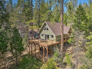 Situated in a forested area, this cabin features a deck with outdoor seating and a covered patio.