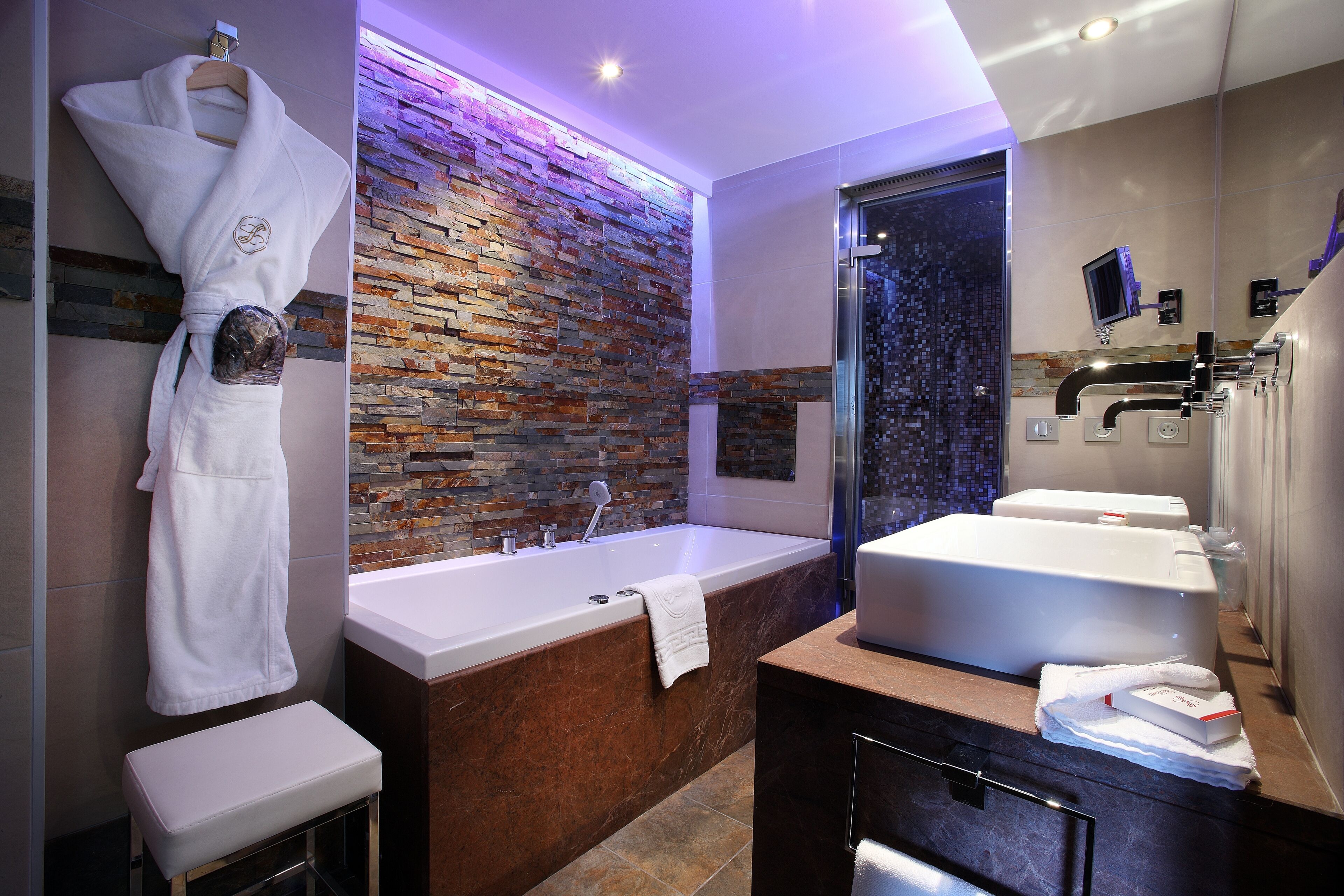 A modern bathroom with a large bathtub, a marble countertop, and a stone wall backsplash.