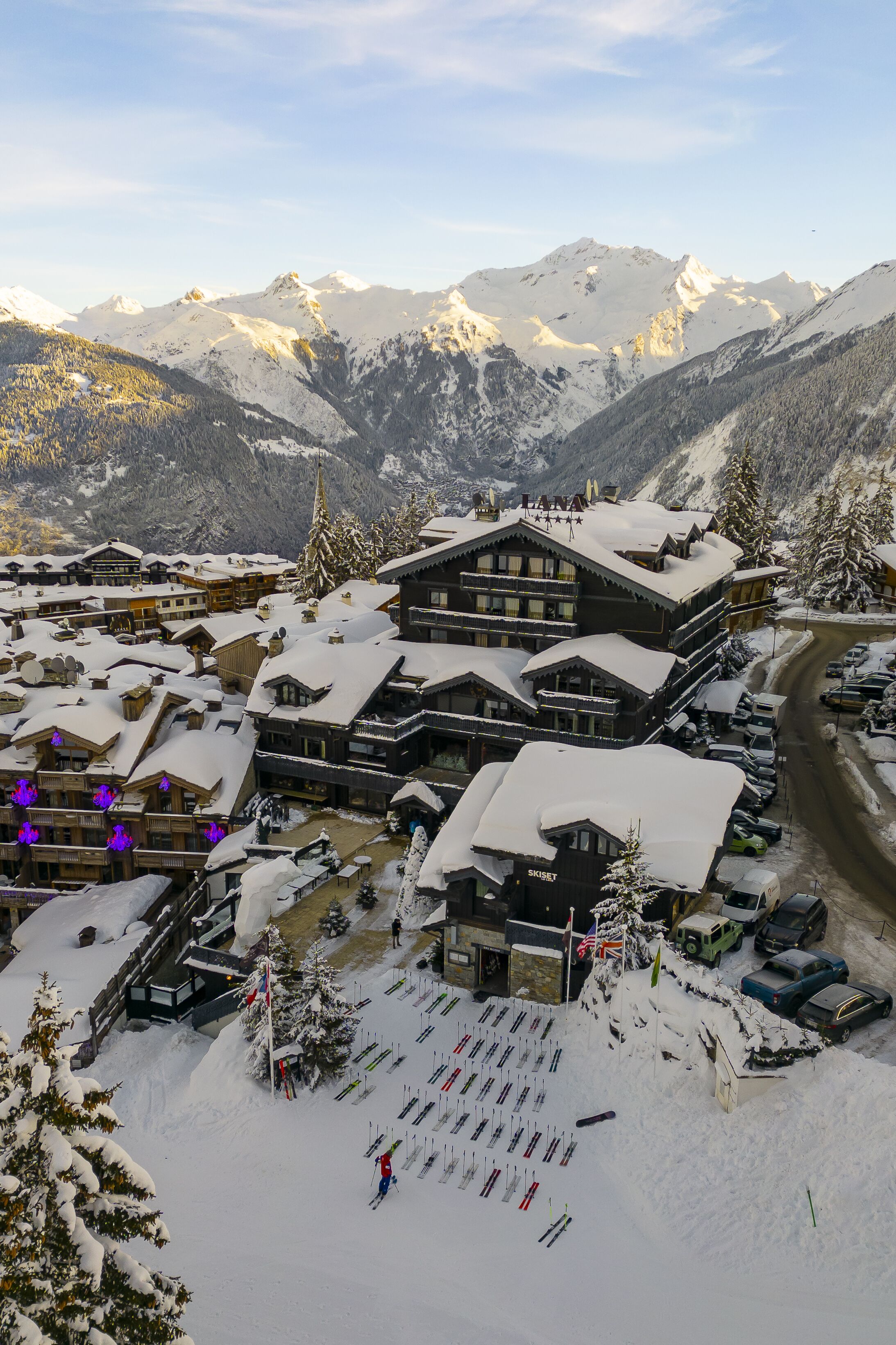 A snow-covered mountain resort with multiple buildings, ski slopes, and a parking area.