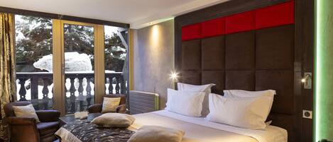 A bedroom with a large bed, a chair, a nightstand, and a view of a balcony with snow-covered trees.