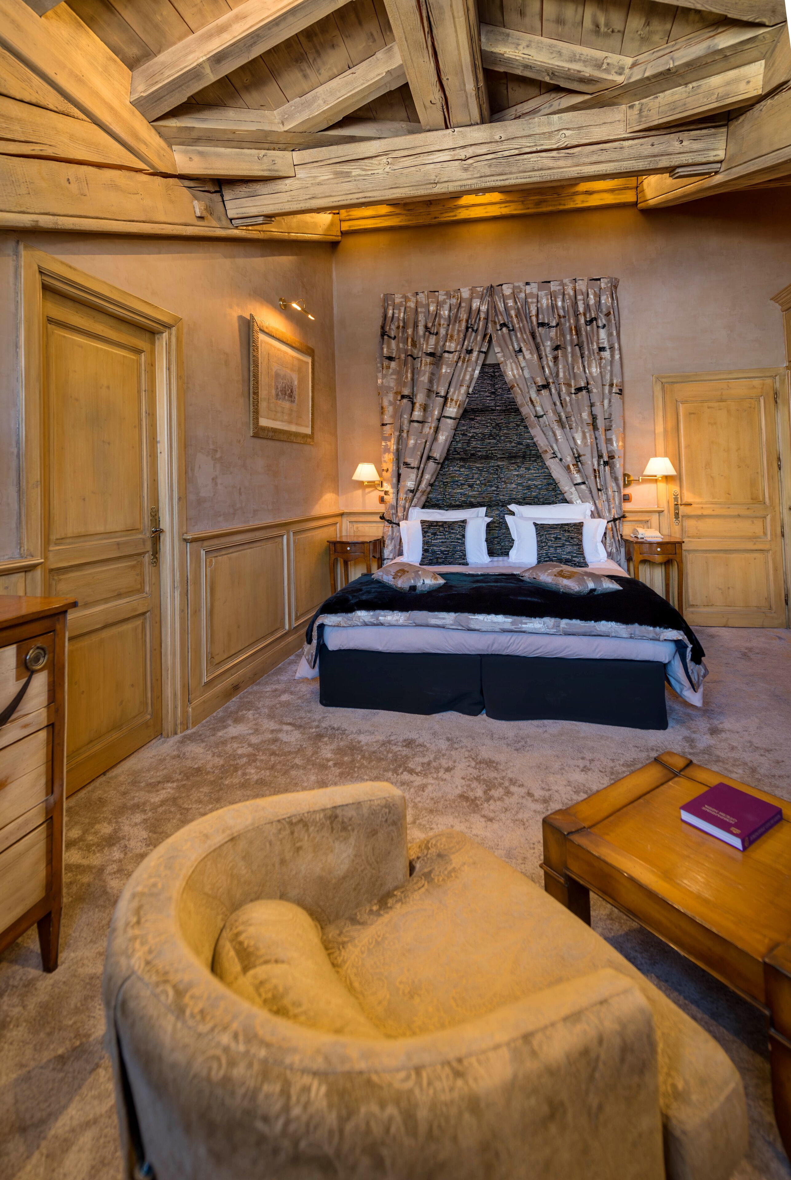 Un dormitorio con una cama grande, cabecero de madera, dos lámparas de noche, una mesita de noche de madera, un sillón redondo y una mesa de centro de madera.