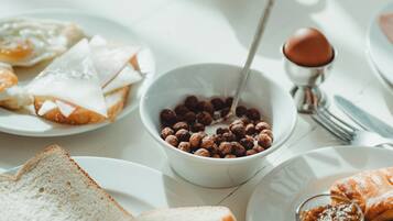 A breakfast table with toast, eggs, a bowl of cereal, a cup of coffee, and a small dish of jam.