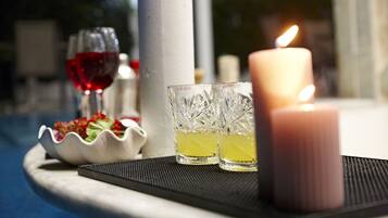Et stearinlys, to glas og en skål med blomster på et bord i nærheden af en pool.