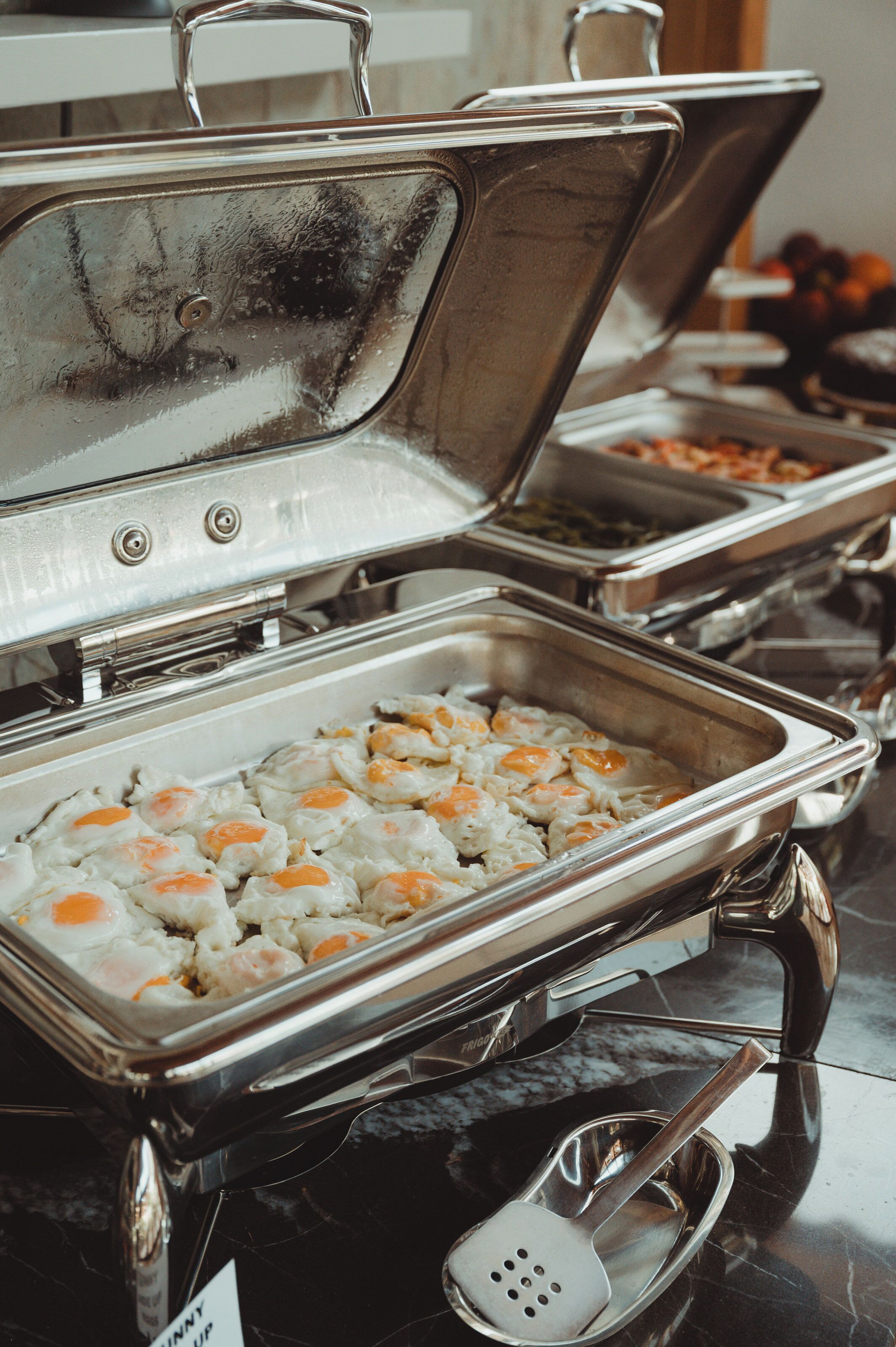 A buffet setup with various food items and a serving spoon.