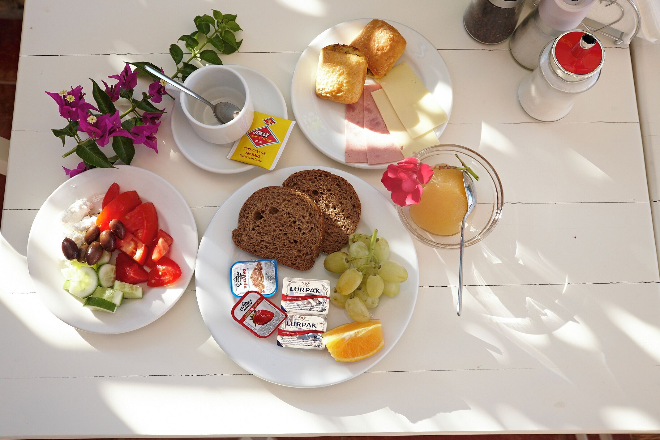 Ein Frühstückstisch mit Tellern voller Speisen, darunter Toast, Käse, Schinken und Obst, sowie Beilagen und ein Glas Saft.