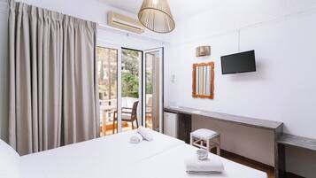 Une chambre d’hôtel équipée d’un lit, d’un bureau, d’une chaise, d’une télévision et d’une porte-fenêtre coulissante donnant sur l’extérieur.
