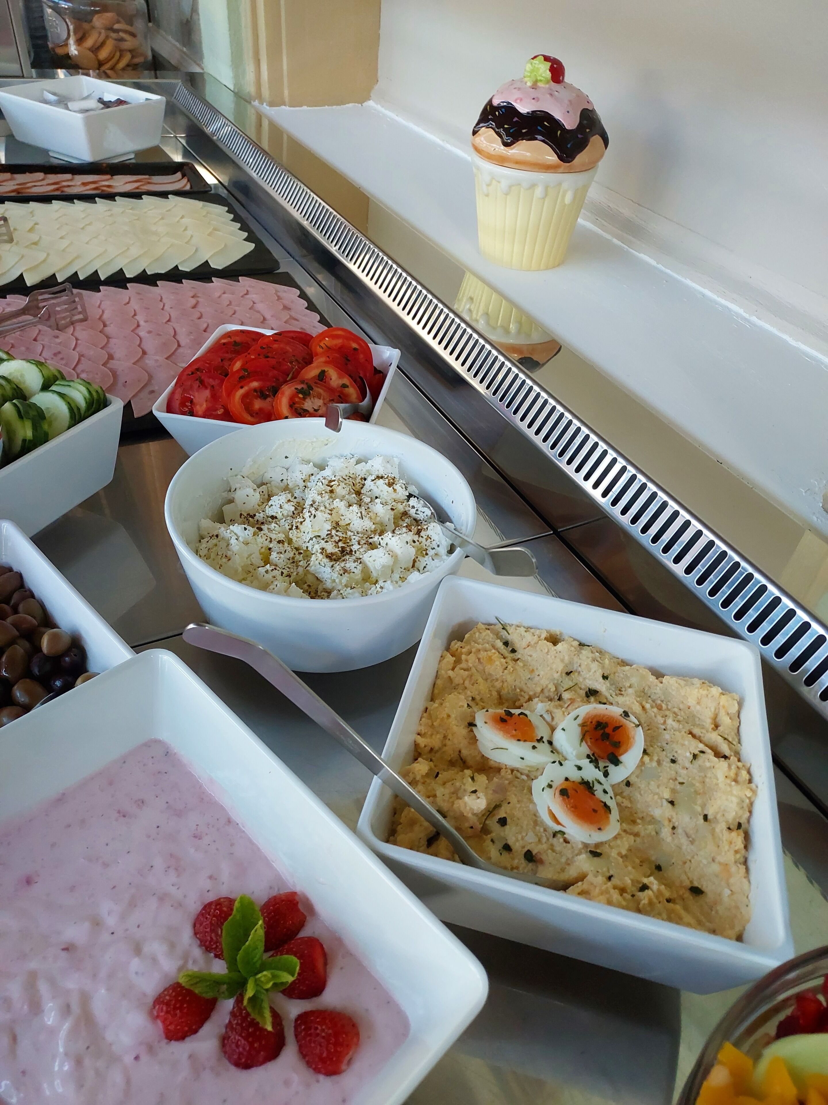 A buffet with various food items including a cupcake, a bowl of salad, and a dish with eggs.