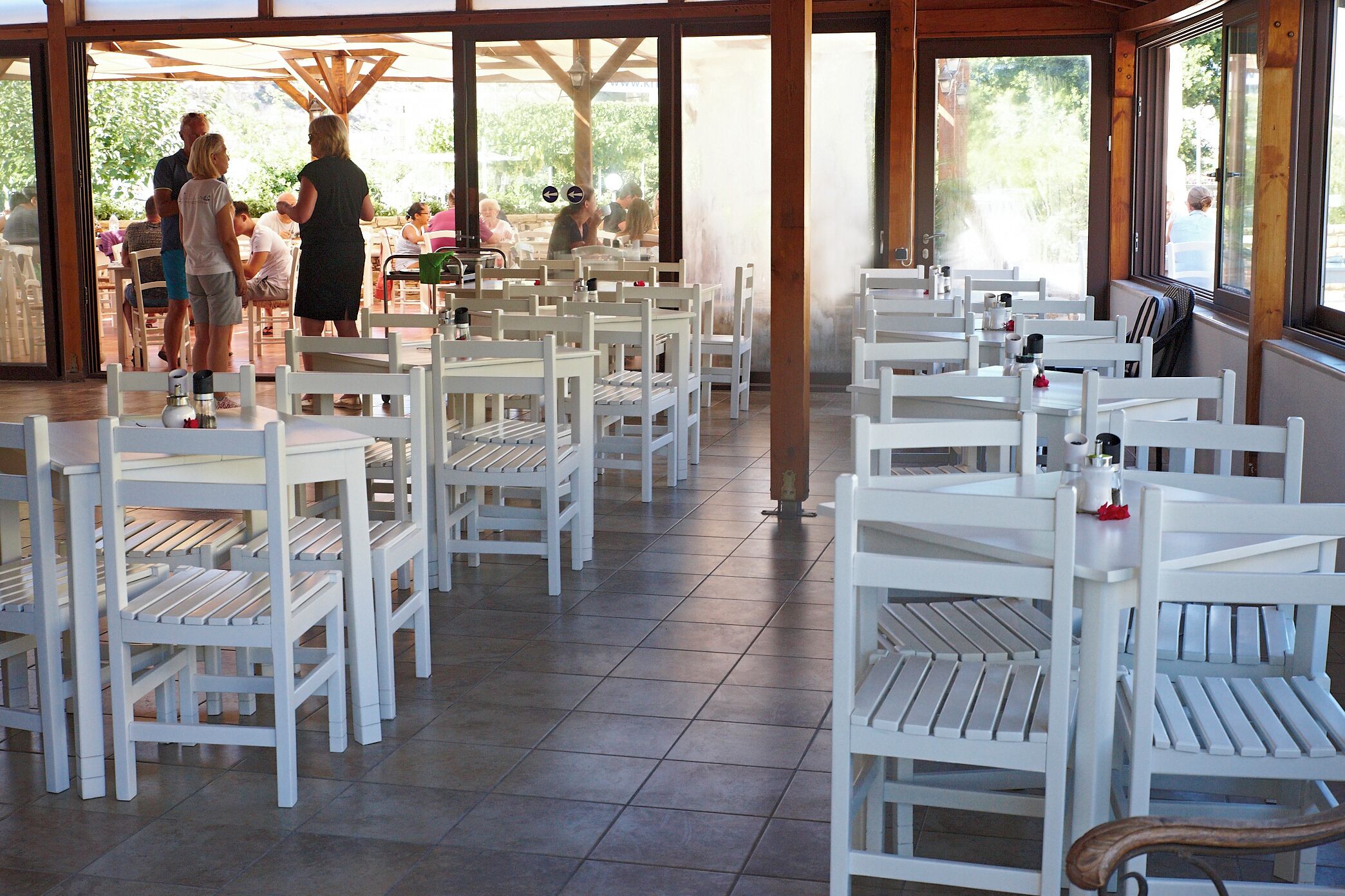 An indoor dining area with white chairs and tables, large windows, and a view of the outdoors.