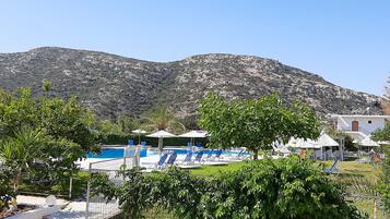 A pool area with lounge chairs and umbrellas, surrounded by greenery and a mountain backdrop.