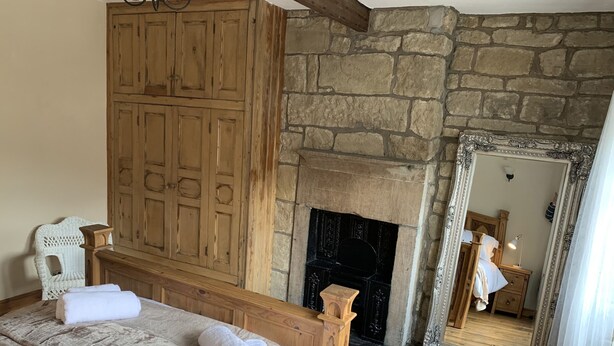 A bedroom with a stone fireplace, wooden wardrobe, and a large mirror. - Meg's Den (Hebden Bridge)