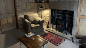 A cozy living room with a stone fireplace, a comfortable armchair, a coffee table, and a rug. - Meg's Den (Hebden Bridge)