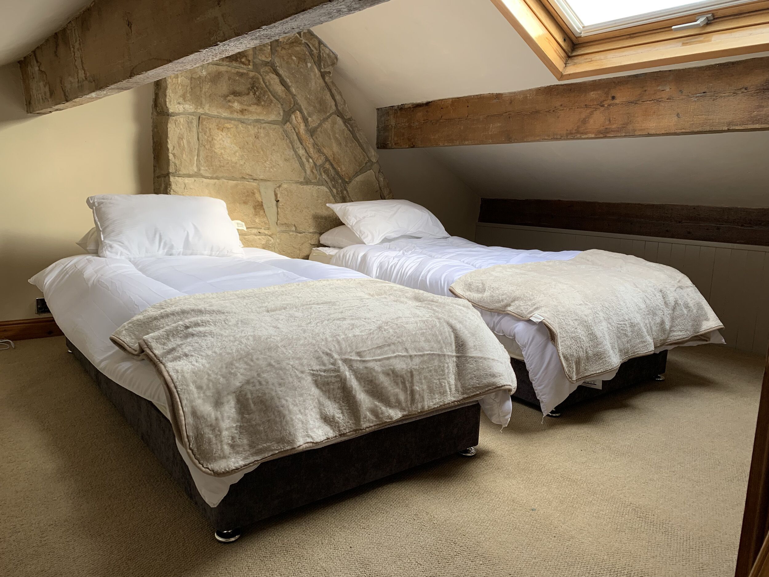 A bedroom with two beds, stone walls, wooden beams, and a skylight.