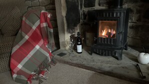 A cozy room with a stone fireplace, a blanket, a wine bottle, and a white teapot. - Meg's Den (Hebden Bridge)