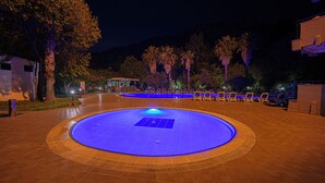 A nighttime swimming pool area with lounge chairs and a building in the background. - Rios Beach Hotel (Kemer)