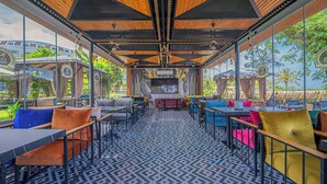An indoor seating area with tables and chairs, a patterned floor, and large windows offering a view of the outdoors. - Rios Beach Hotel (Kemer)