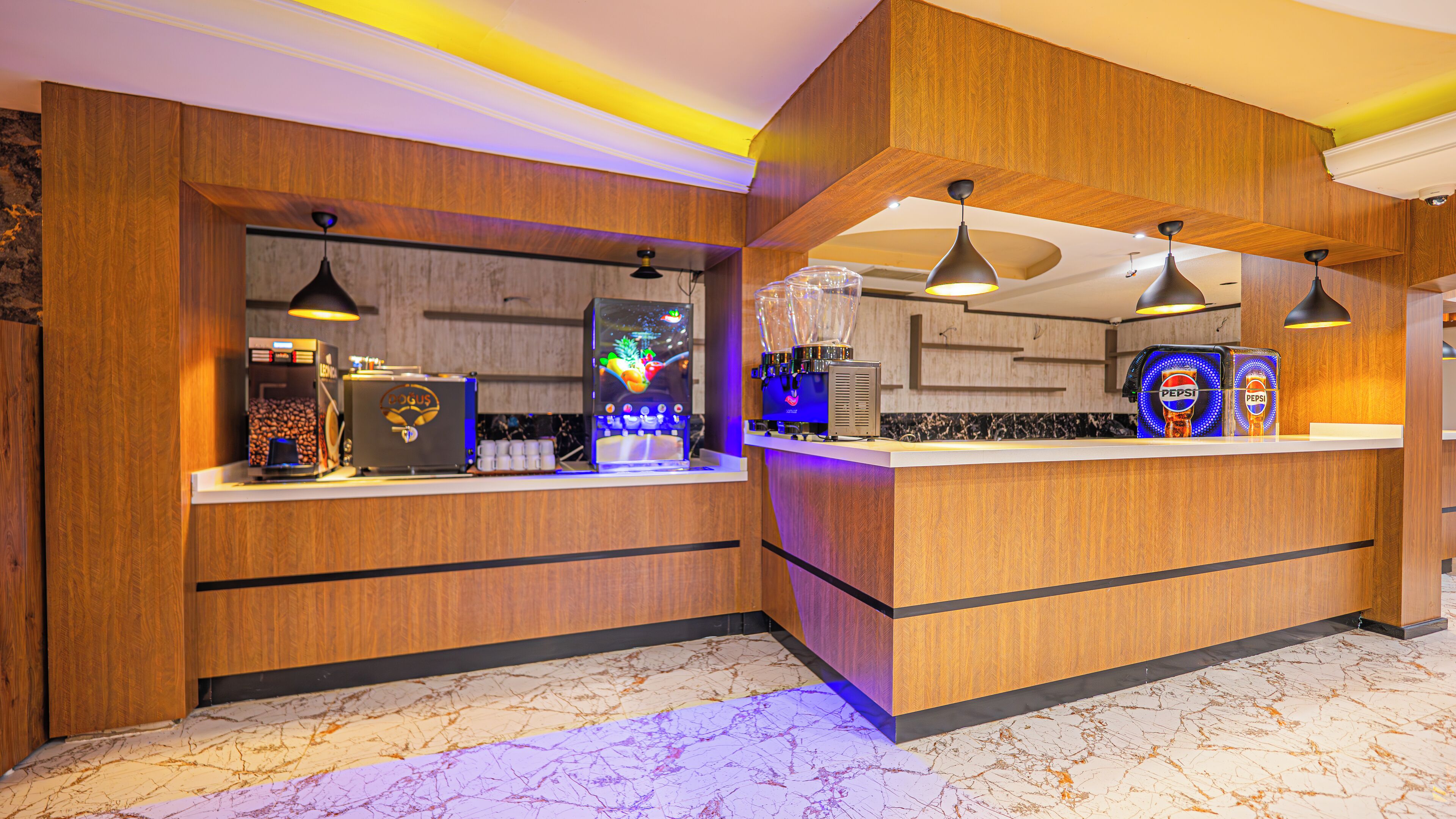 A modern bar area with wooden paneling, a marble floor, and a variety of beverage dispensers including coffee machines and Pepsi refrigerators.