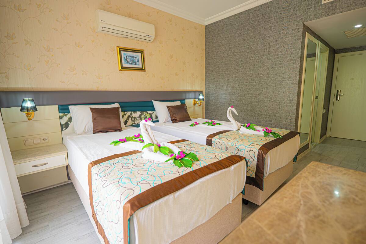 A hotel room with two beds, a nightstand, a lamp, and a picture on the wall.