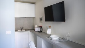 Een compacte keuken met een ingebouwd spoelbakje, een broodrooster, een koffiezetapparaat en een flatscreen televisie aan de muur.