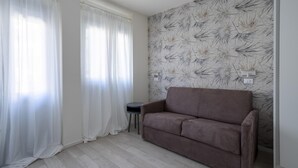 Een kamer met een bank, een klein rond tafeltje en een wand met een bloemenpatroon.