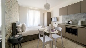 A modern hotel room with a bed, a small dining table, a TV, and a kitchenette. - Italianway - The B Village Superior - 44 (Milan)