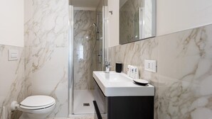 A modern bathroom with a white toilet, a glass-enclosed shower, and a white sink with a black cabinet. - Italianway - The B Village Superior - 44 (Milan)