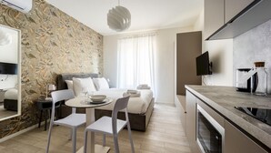 A modern hotel room with a bed, a dining area, a kitchen, and a large window with curtains. - Italianway - The B Village Superior - 44 (Milan)