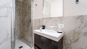 A modern bathroom with a glass-enclosed shower, a white sink with a black soap dish, and a marble-tiled wall. - Italianway - The B Village Superior - 44 (Milan)