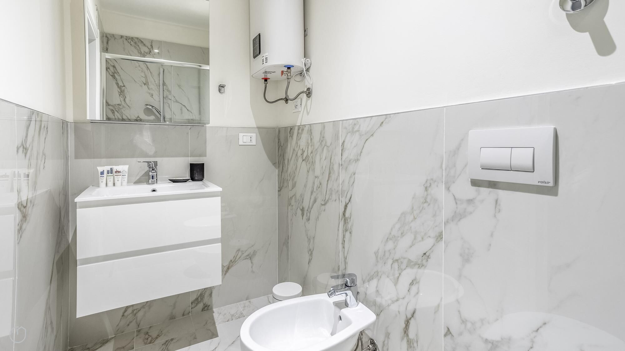 A modern bathroom with a marble backsplash, a white sink, a mirror, and a toilet.