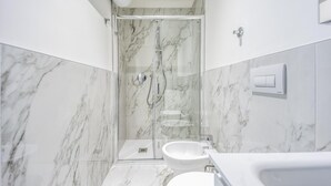 A modern bathroom with a glass-enclosed shower, a white sink, and marble walls. - Italianway - The B Village Superior - 46 (Milan)