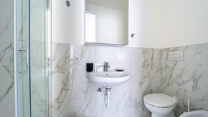 A modern bathroom with a glass shower enclosure, a white sink with a marble backsplash, and a toilet. - Italianway - The B Village Superior - 50 (Milan)