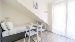 A small, neatly arranged bedroom with a bed, a table with chairs, and a window with curtains. - Italianway - The B Village Superior - 50 (Milan)
