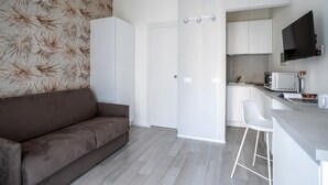 A modern apartment with a brown sofa, a kitchen with a TV, and a white door.