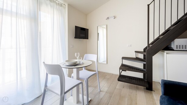 Un salon moderne avec un escalier, un coin repas comprenant des chaises et une table, et un téléviseur fixé au mur.