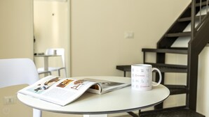 Une table avec un magazine et une tasse dessus, une chaise blanche et un escalier en arrière-plan.
