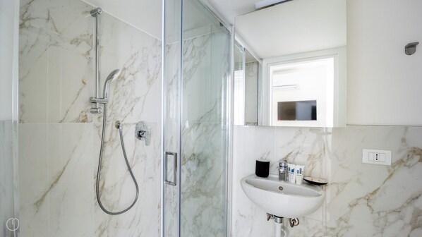 Un baño moderno con ducha envuelta en cristal, un lavabo blanco y un espejo encima.